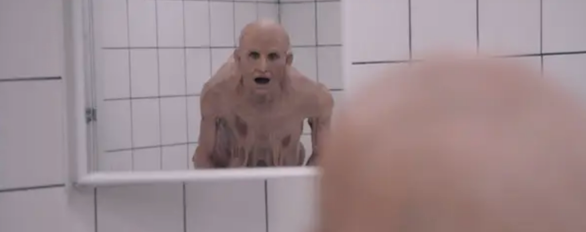 Demi Moore as a bald, melting creature staring into a bathroom mirror