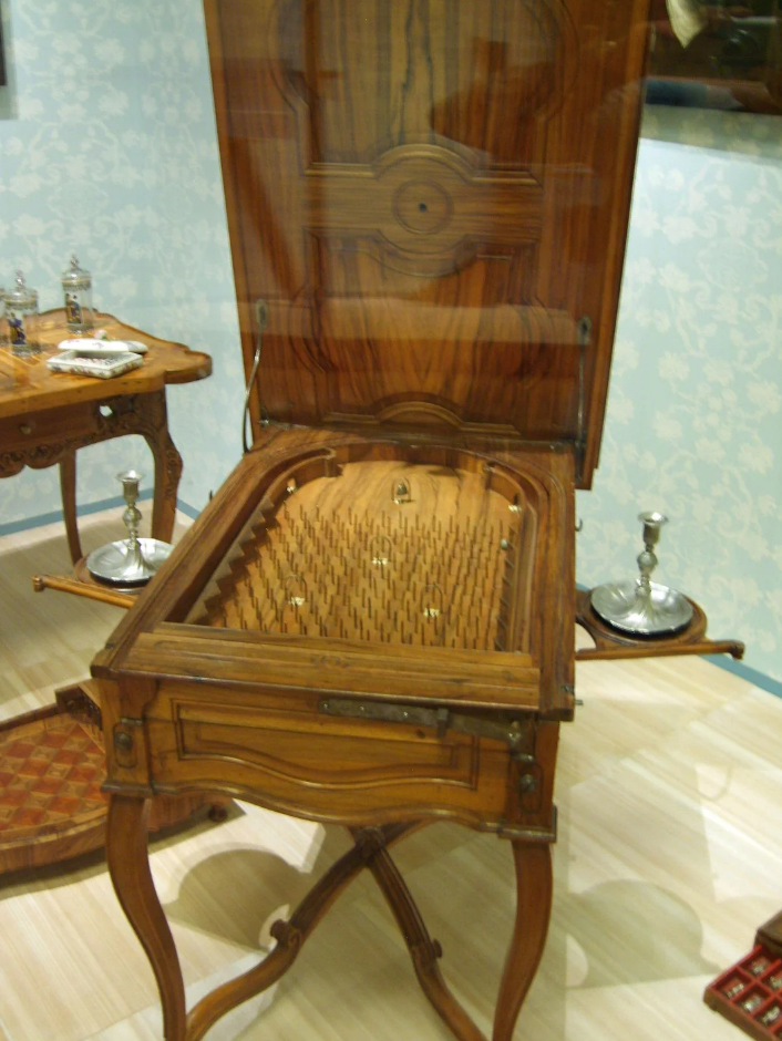 Antique wooden bagatelle game table with a pinball setup, open lid, and ornate legs on display in a museum setting