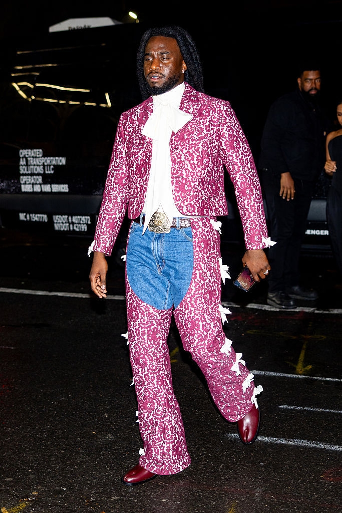 Persona en la calle con traje de inspiración vaquera, sobre pantalones de mezclilla. Lleva una chaqueta y botas elegantes