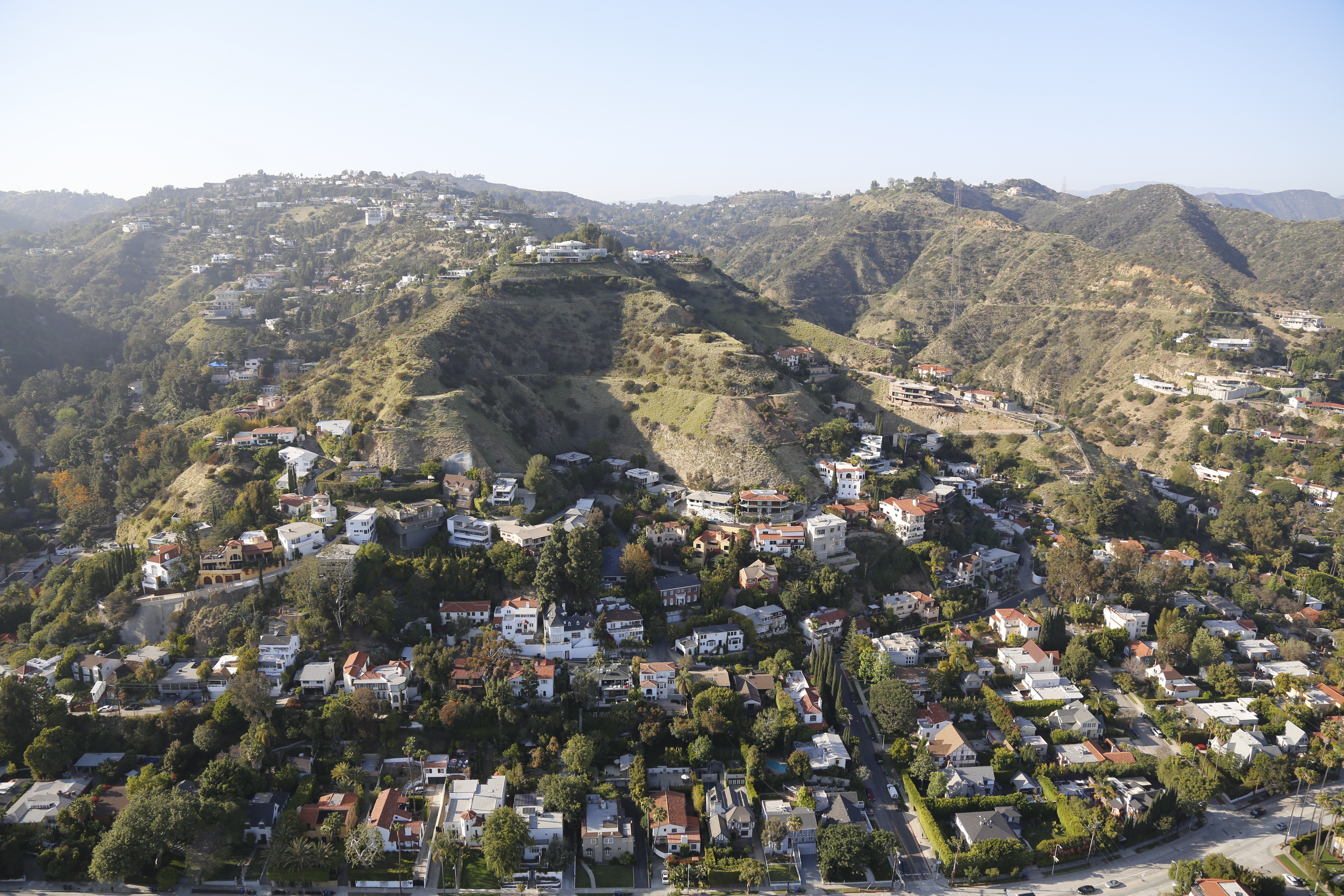 Aerial view of a residential area in hilly terrain with houses surrounded by vegetation and winding roads