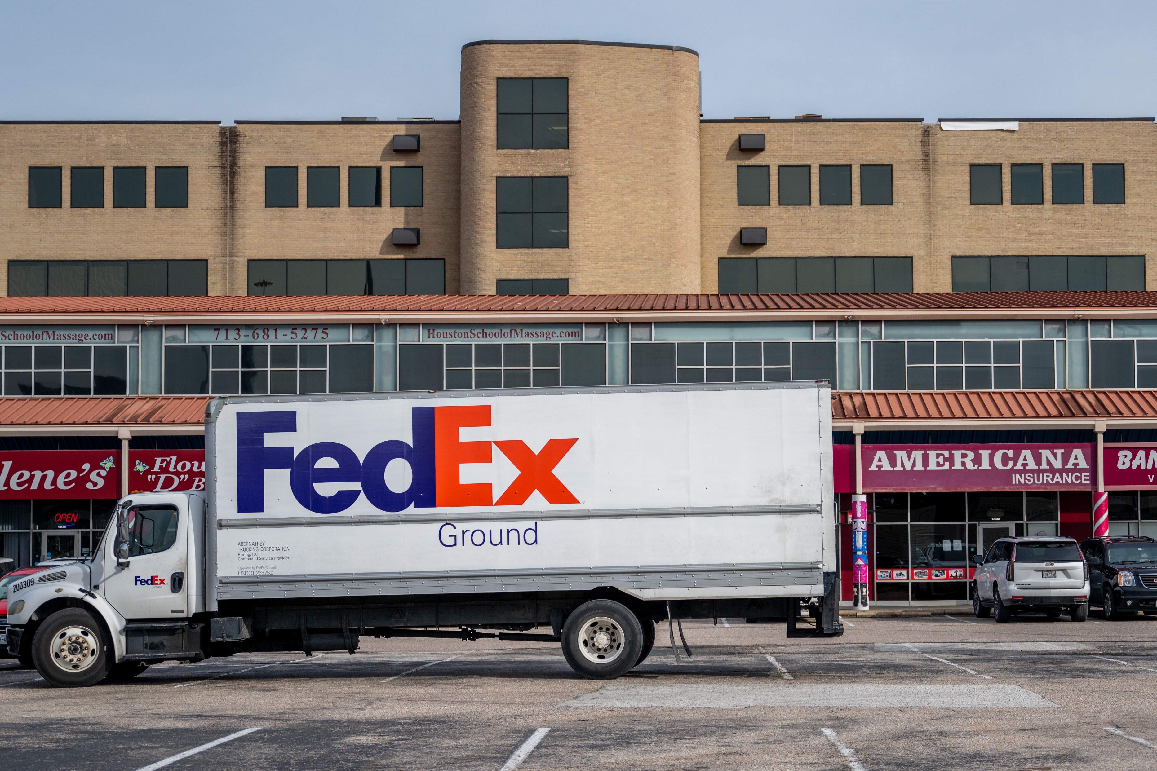 FedEx Ground delivery truck parked in front of a commercial building with various storefronts