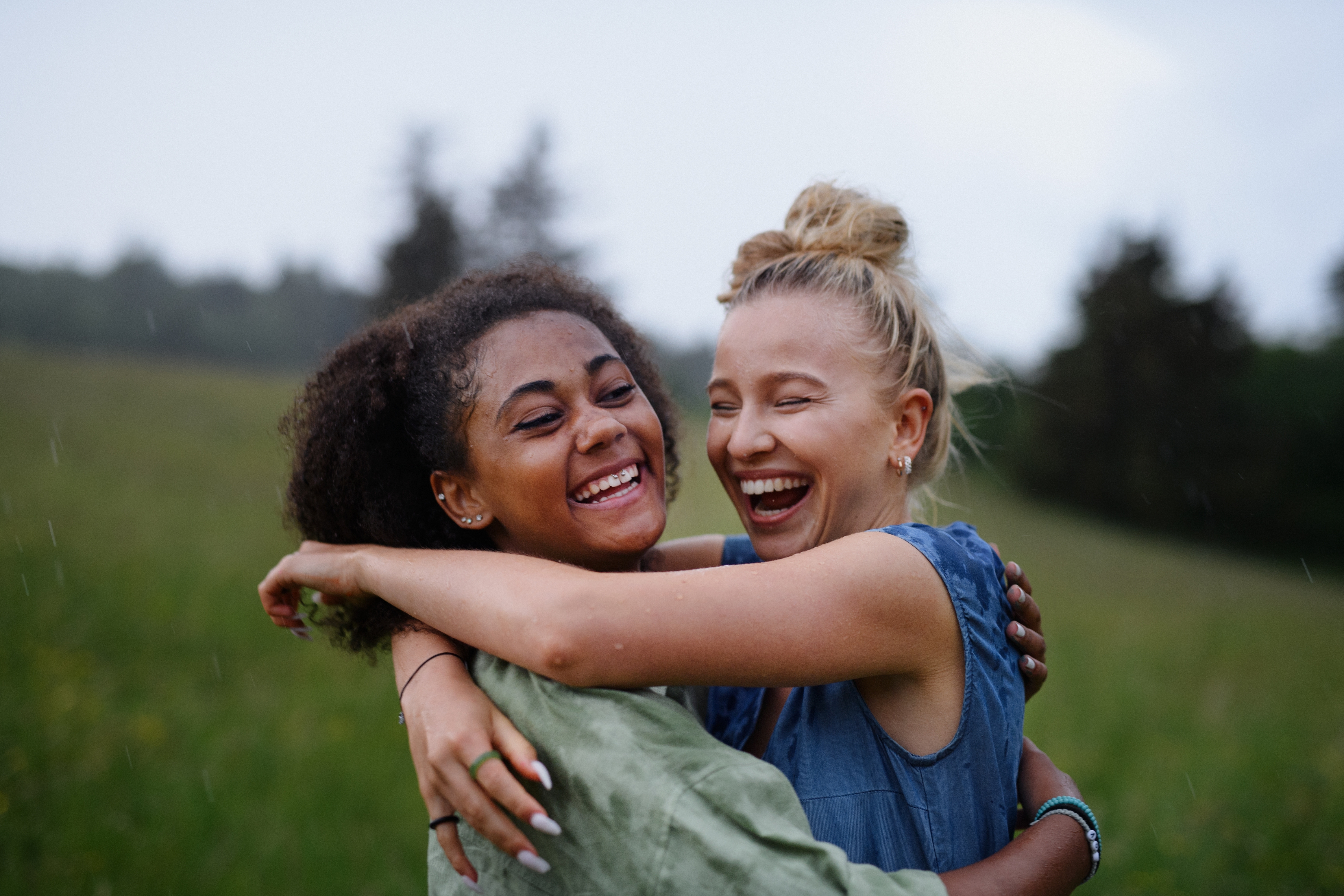 Two people embracing and laughing together in an outdoor setting. Their joyful expression conveys a sense of friendship and happiness