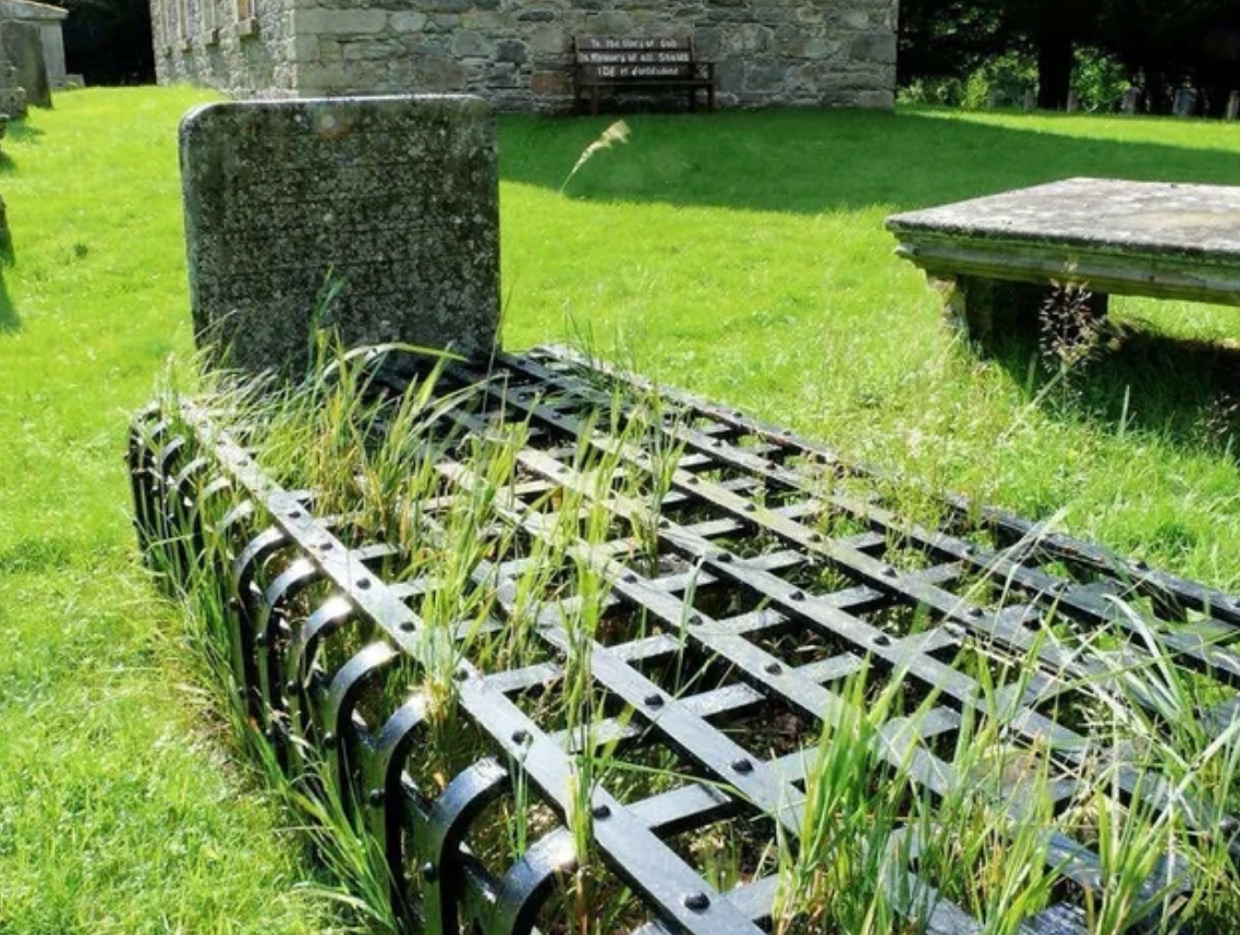 Grave with iron cage in a grassy cemetery, likely a historical "mortsafe" to prevent body snatching