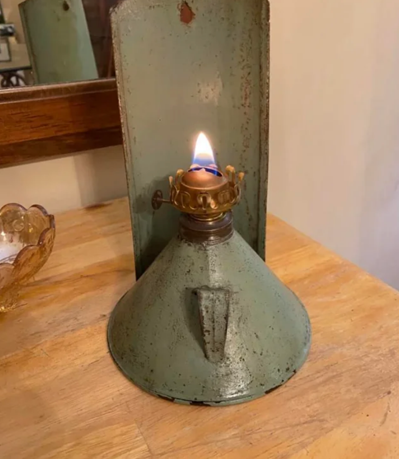 An antique oil lamp with a lit flame sits on a wooden surface, next to a decorative glass bowl