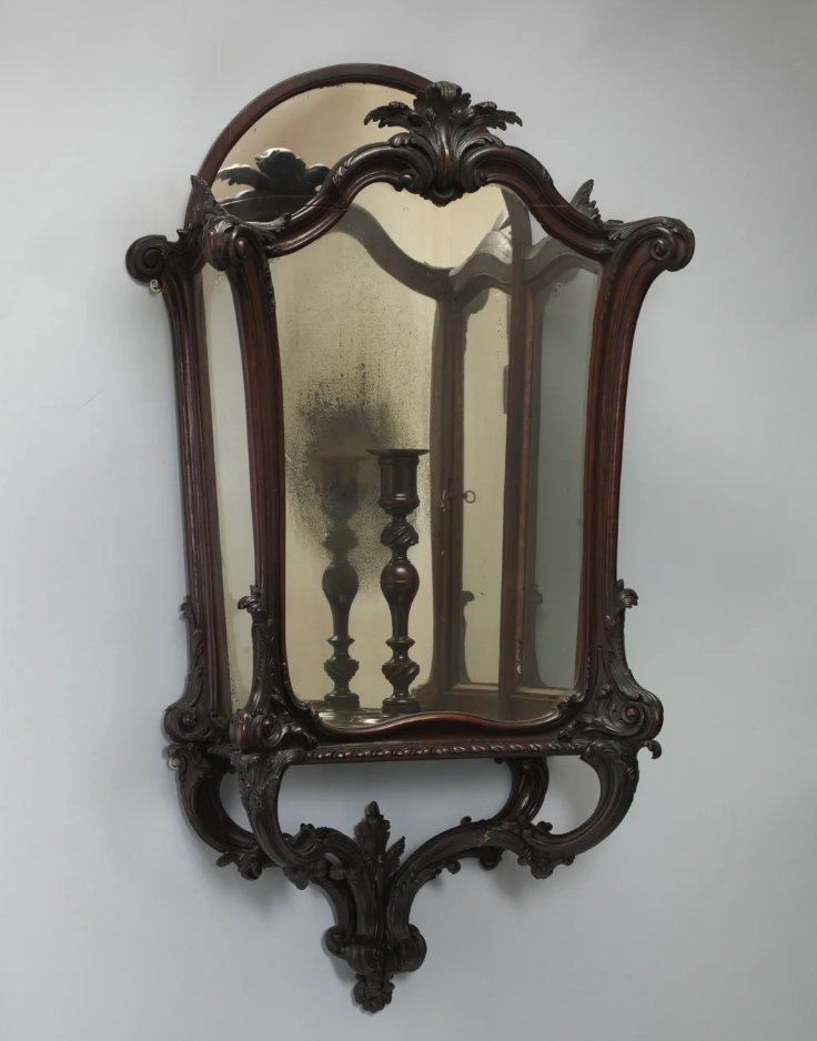 Ornate vintage mirror with intricate wood detailing, reflecting a candle holder