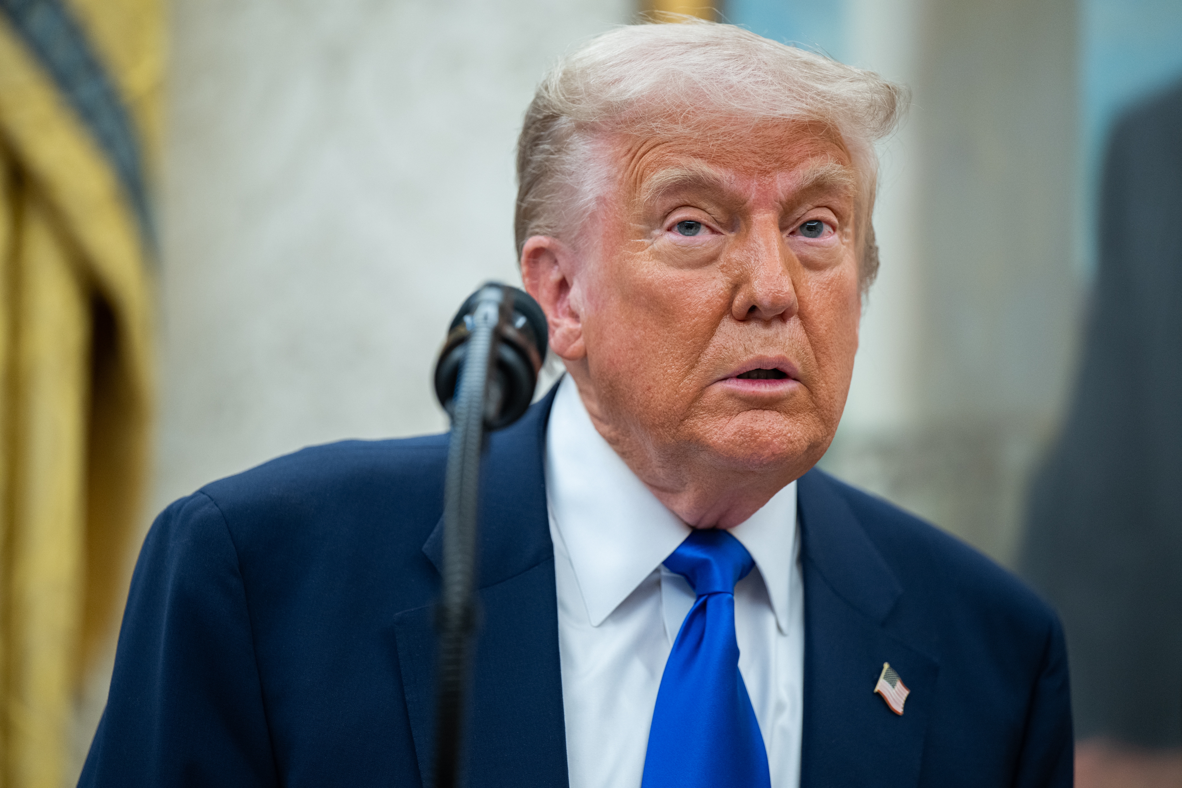 Donald Trump in a suit and tie stands near a microphone, looking ahead