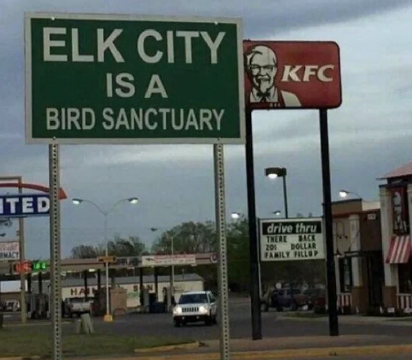 Sign in Elk City states it's a bird sanctuary; nearby is a KFC and fast-food area