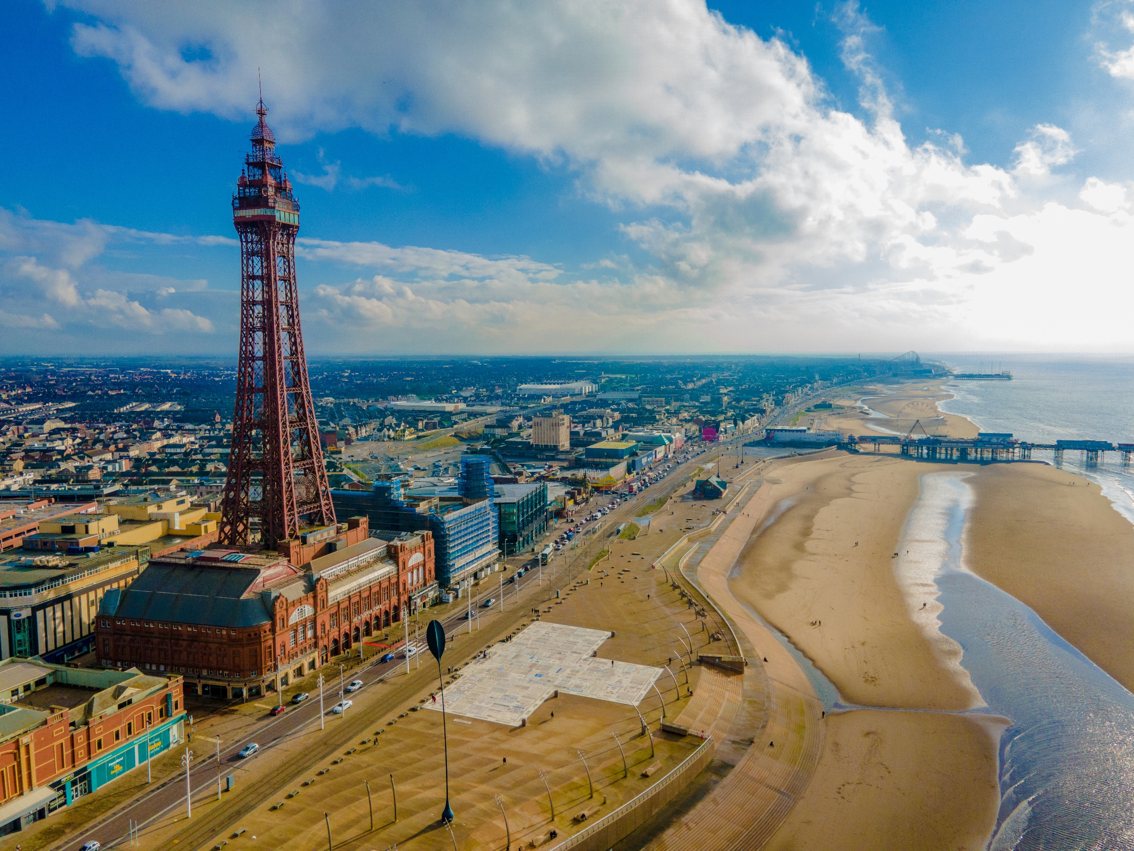 Aerial view of Blackpool Tower by the beach, with the promenade and ocean visible under a partly cloudy sky
