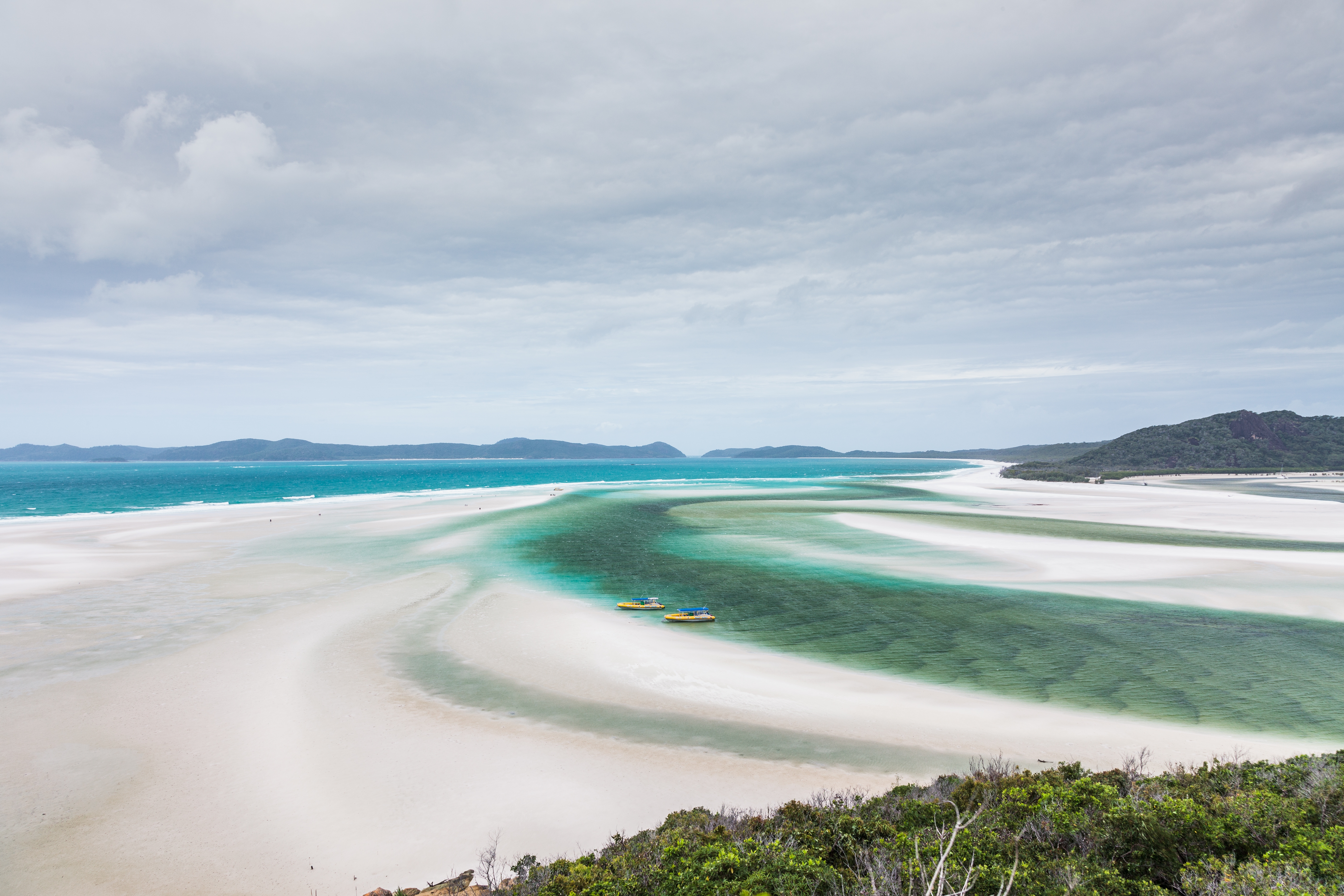 Scenic view of a vast beach with turquoise water winding between sandbanks under a cloudy sky