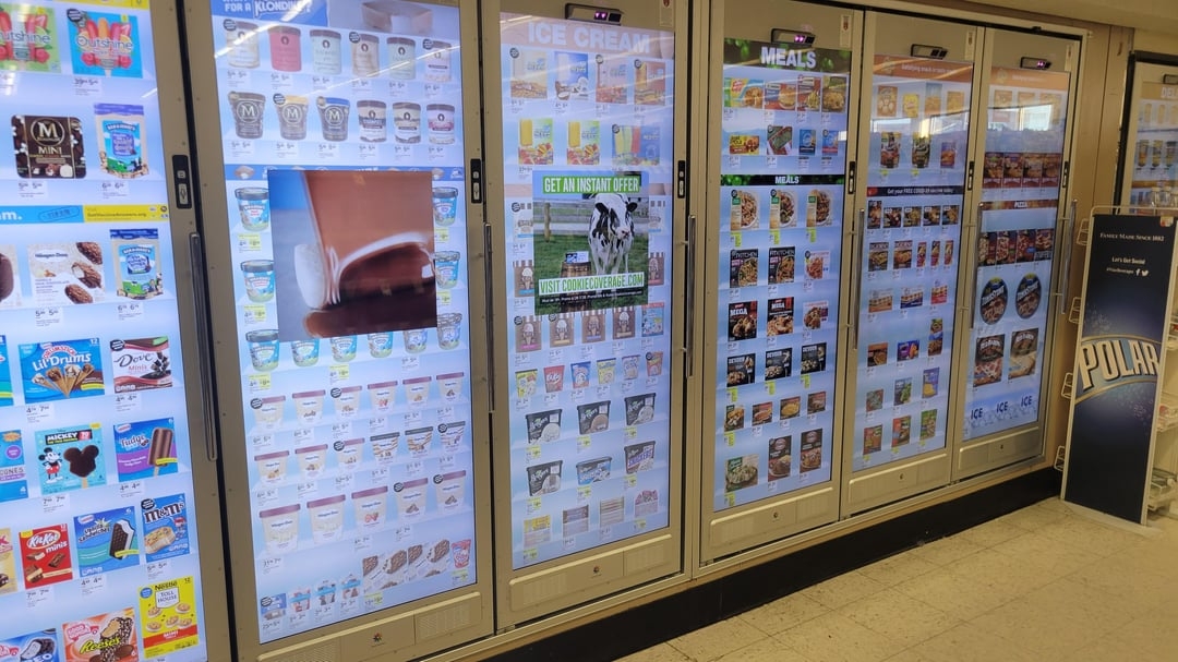 Store freezer aisle displaying various ice cream and meals with digital screens showcasing product ads and promotions