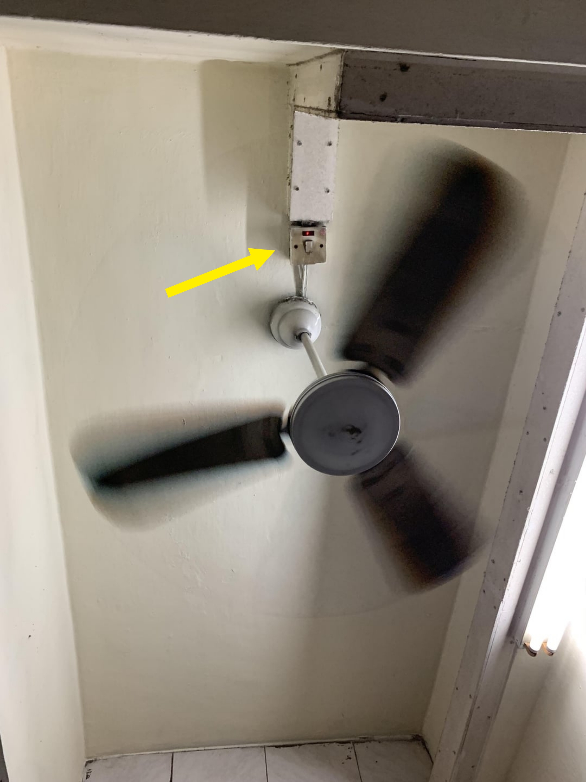 Ceiling fan spinning swiftly in a simple room with a fluorescent light on the wall