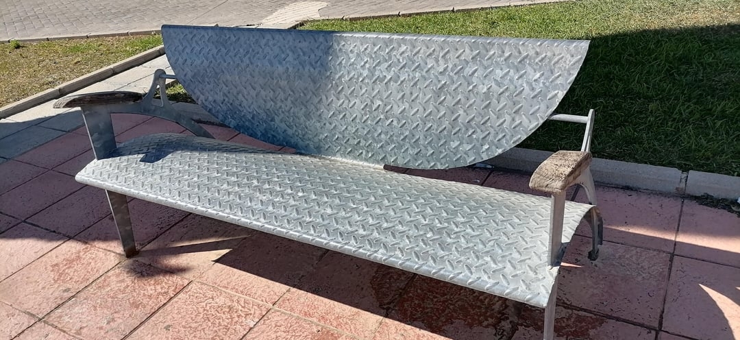Metal outdoor bench with geometric design, featuring angled back and armrests, set on a tiled patio near a grassy area