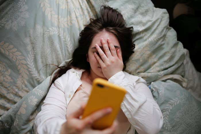 Person lying connected  a bed, holding a phone, with 1  manus  covering their look   successful  evident  vexation  oregon  disbelief