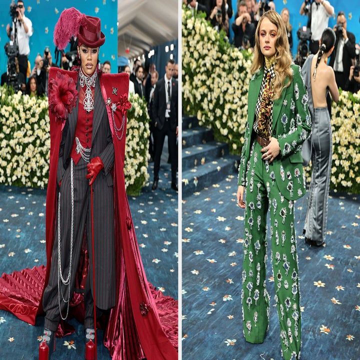 Two people on a red carpet: one in a red, regal ensemble with ornate details; the other in a green, patterned suit with a bold top