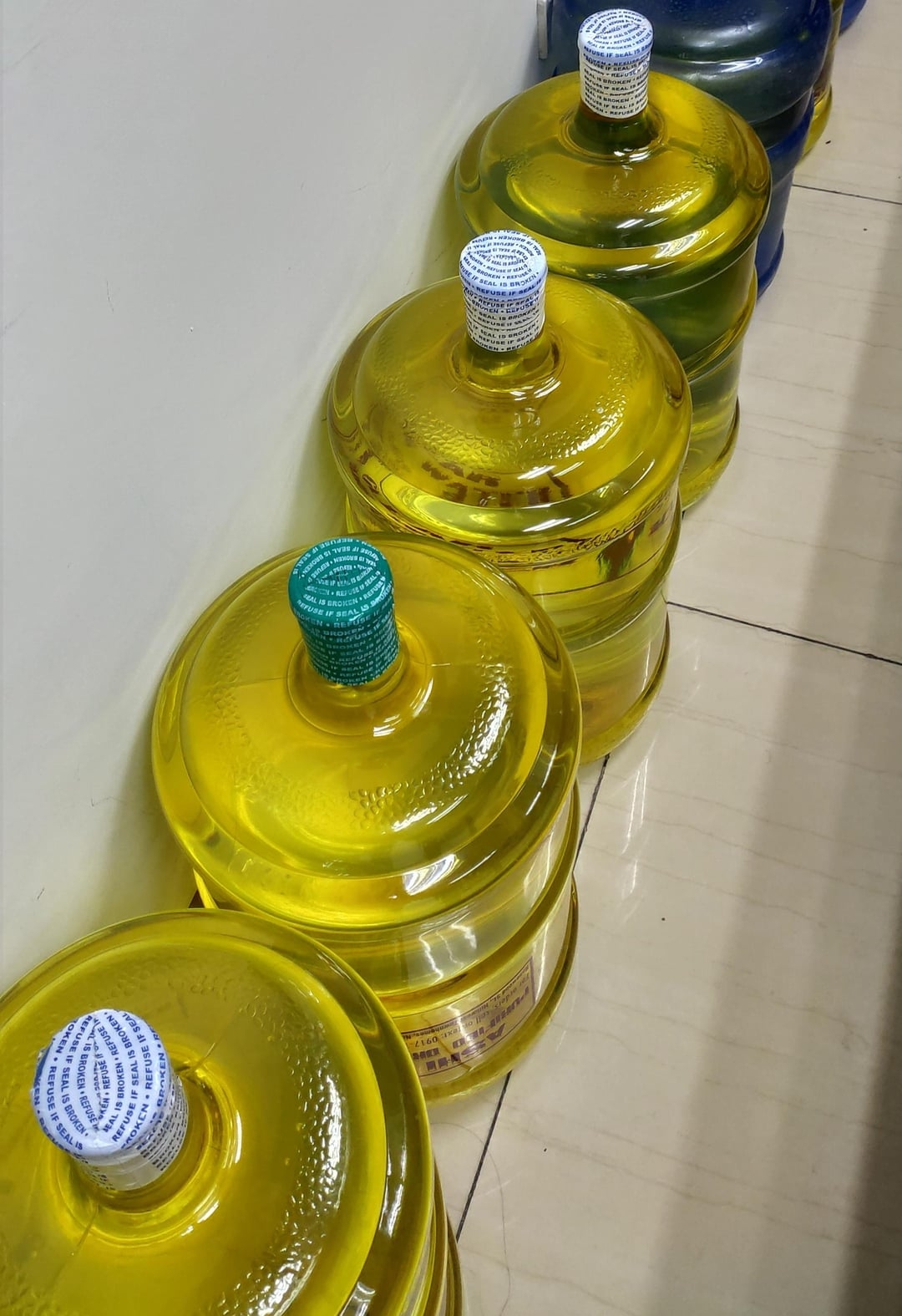Several large water bottles with seemingly yellow liquid, that's actually just water, are lined up against a wall on a tiled floor