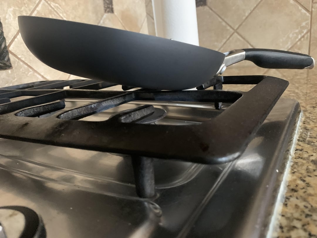 A frying pan balanced precariously on the edge of a stove burner