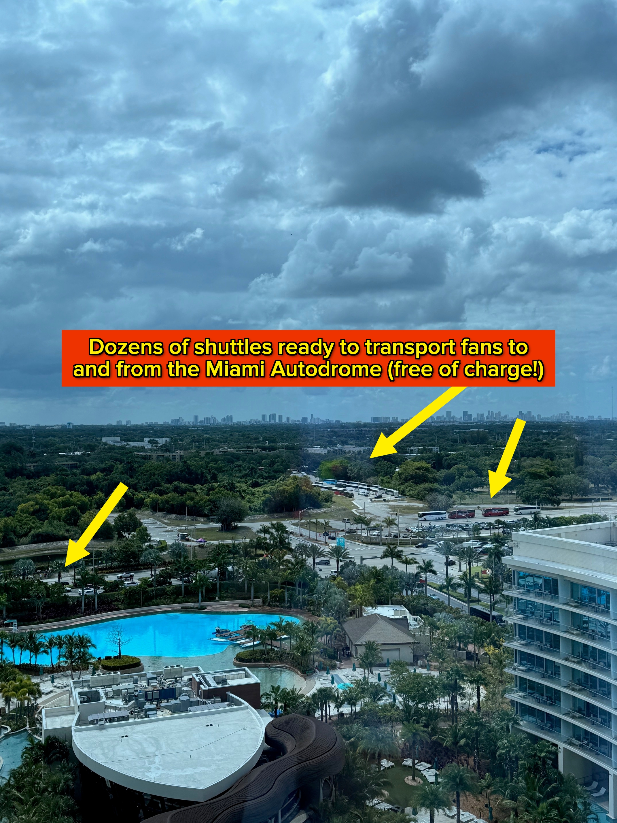 View from a high-rise showing lush greenery, distant city skyline, and a resort-style pool area, under a cloudy sky
