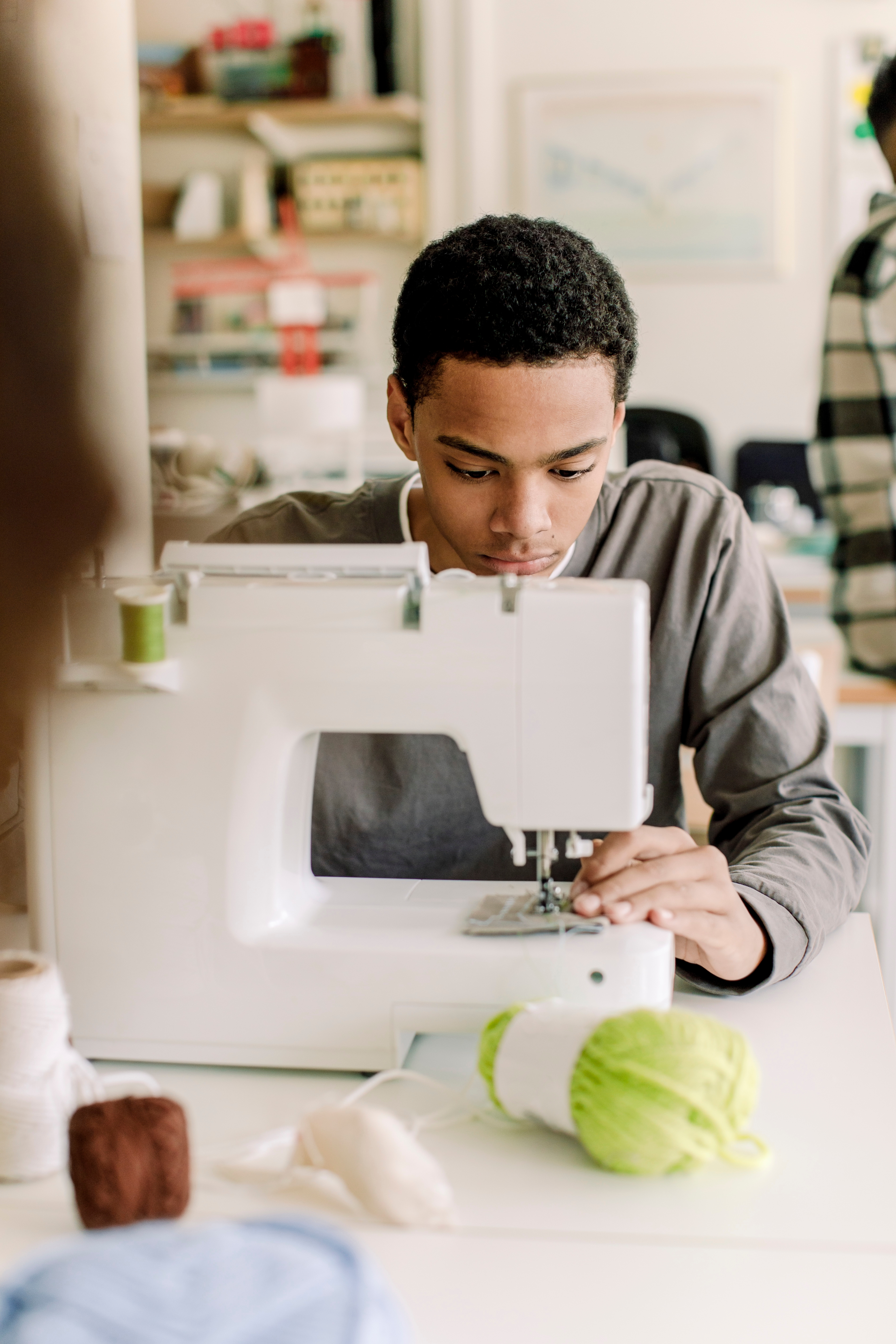 Person sewing at a machine, focused on the task, with crochet threads and yarn nearby on the table