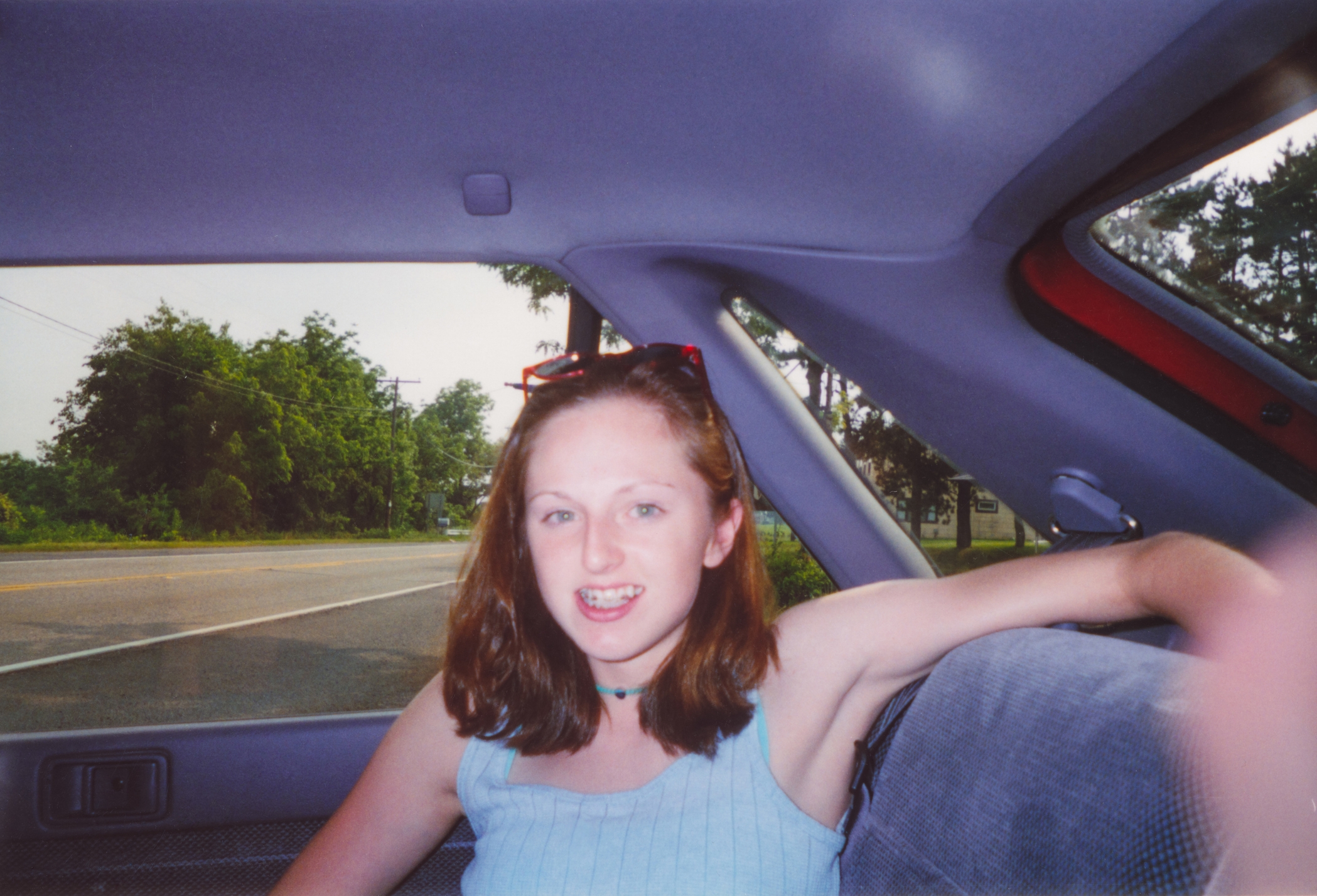 A teenager with medium-length hair sits in the backseat of a car, looking at the camera with a relaxed expression