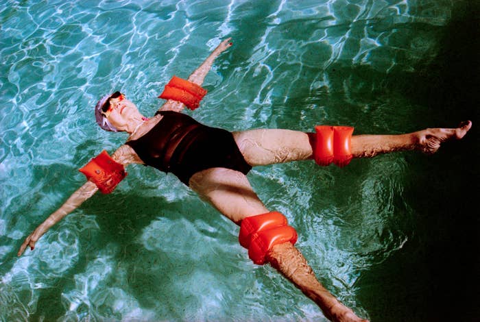 Person floating in a pool wearing a black swimsuit and inflatable arm and leg floats, conveying a relaxed and playful atmosphere