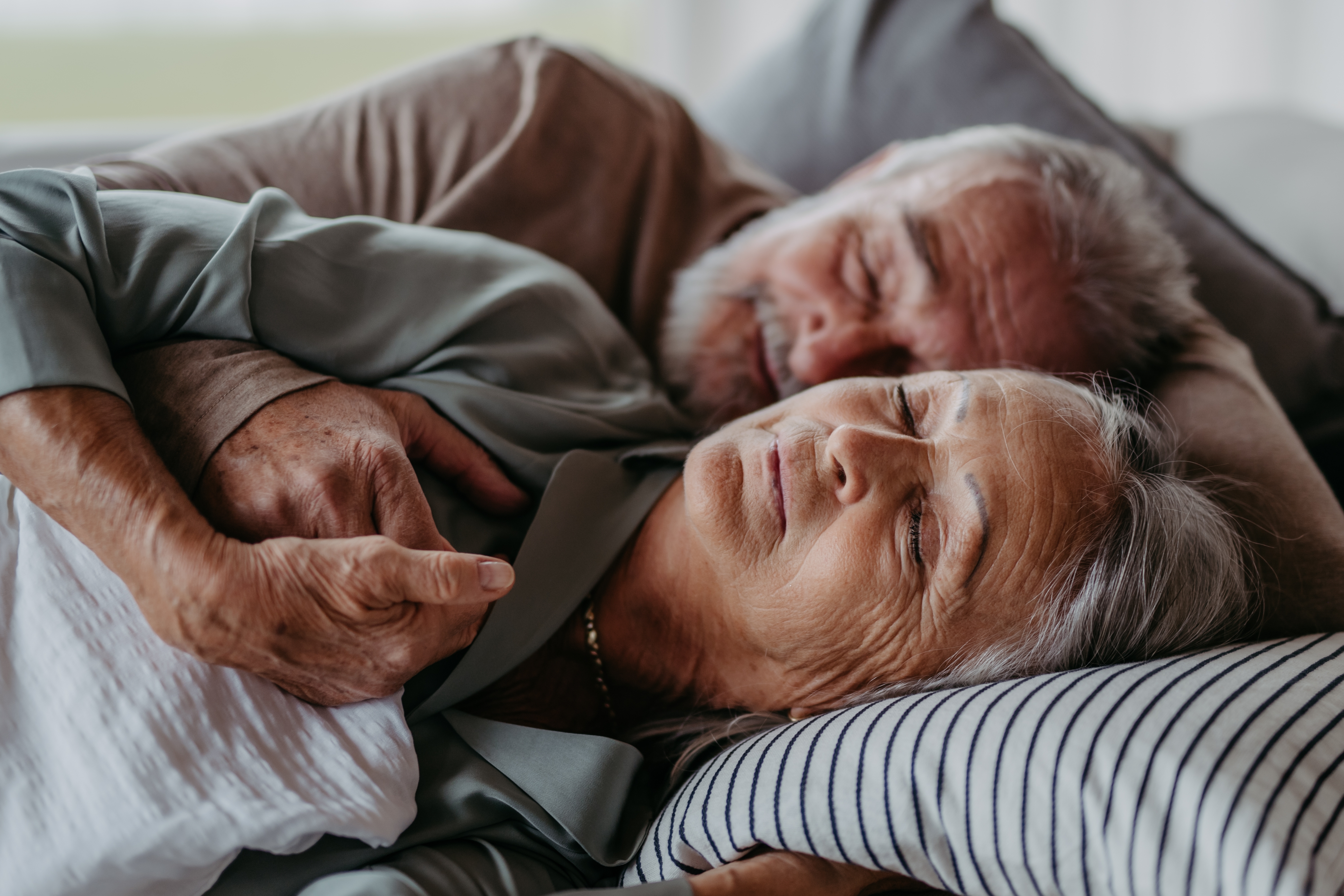 Older couple peacefully resting together in bed, embracing each other with content expressions
