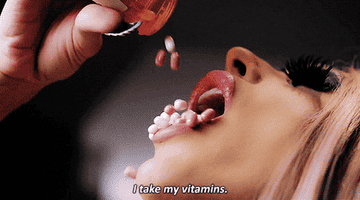 Woman catching vitamins in her mouth from a pill bottle, text at bottom reads: "I take my vitamins."
