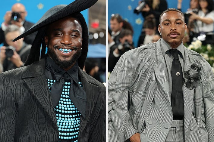 Two individuals on a red carpet, one in a wide-brim hat and polka-dot shirt, the other in a plaid suit with a floral brooch