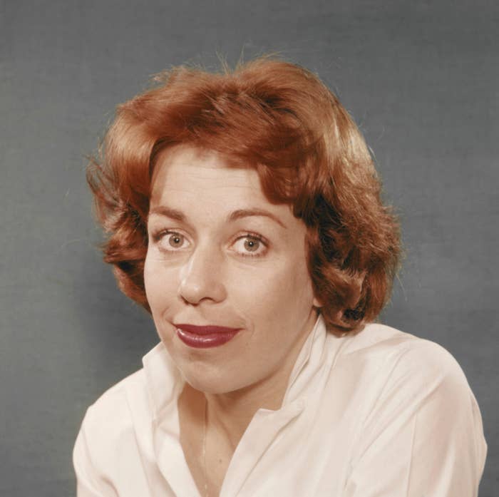 Person with short wavy hair, wearing a white shirt, smiles gently while looking at the camera