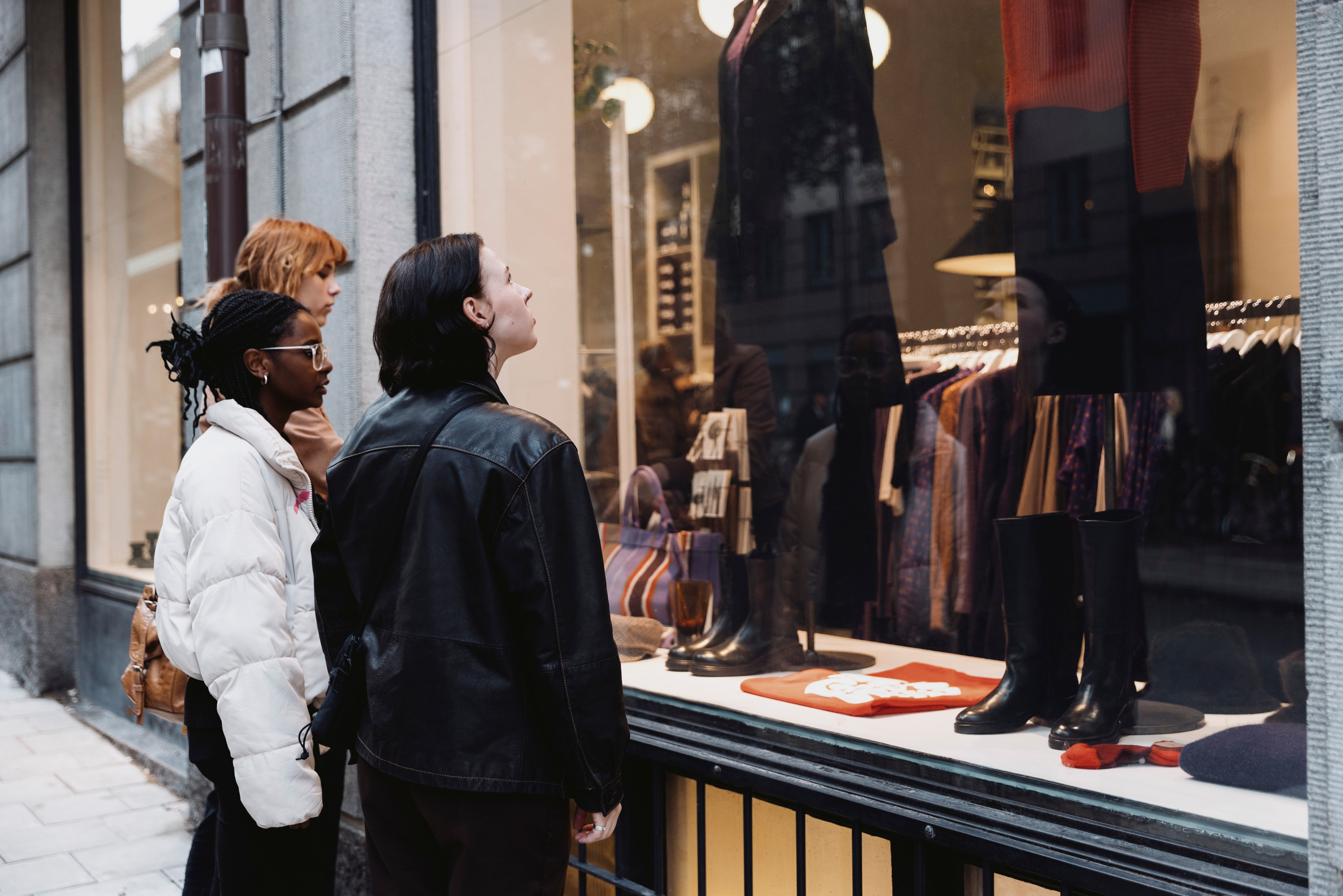 Three people admire stylish outfits displayed in a store window