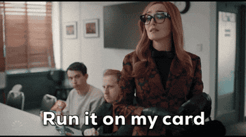 A stylish woman in glasses confidently hands a card to a cashier, saying "Run it on my card," while two people sit in the background