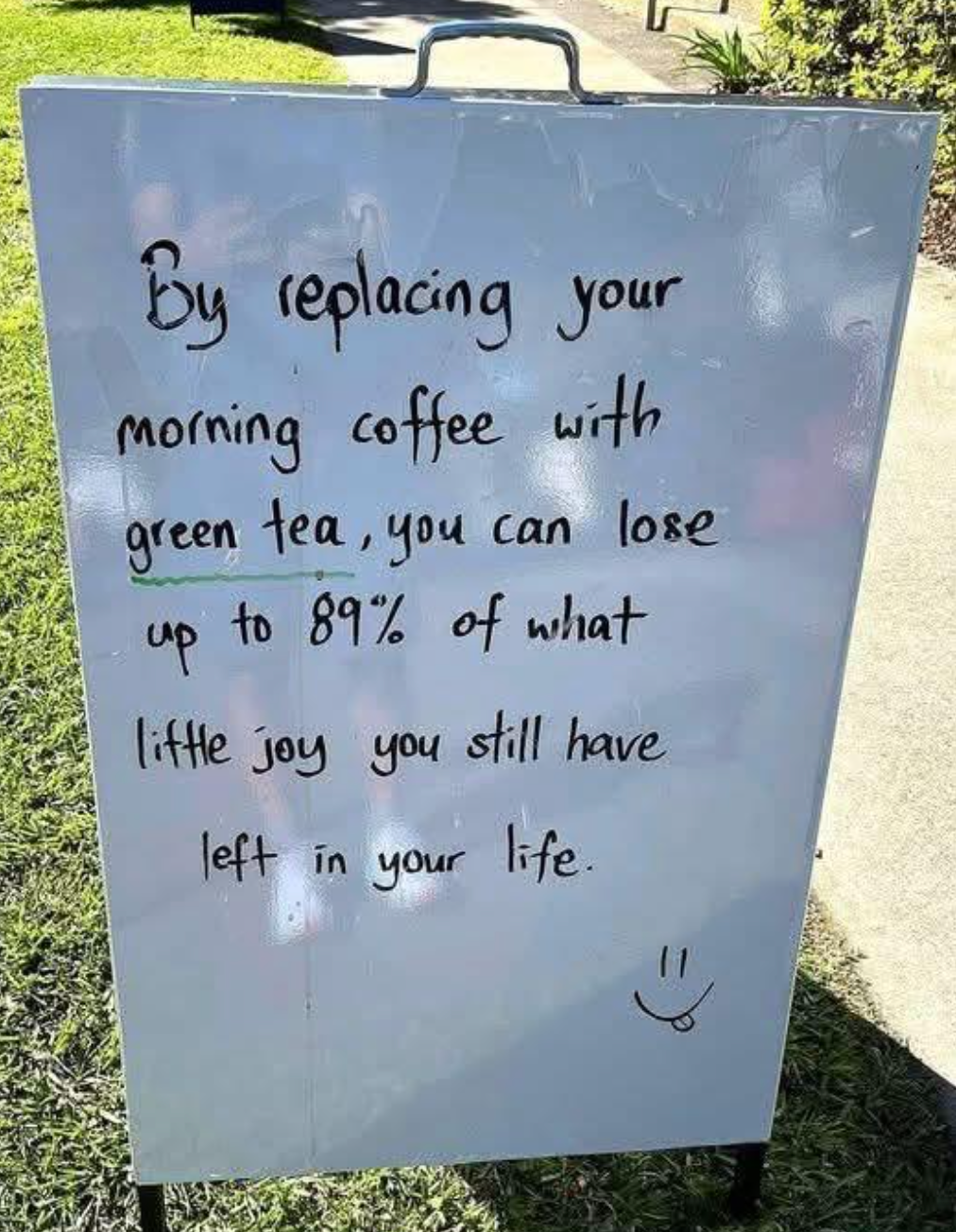 Sign with handwritten text: Replacing morning coffee with green tea may reduce life joy by 89%. Smiley face at the bottom