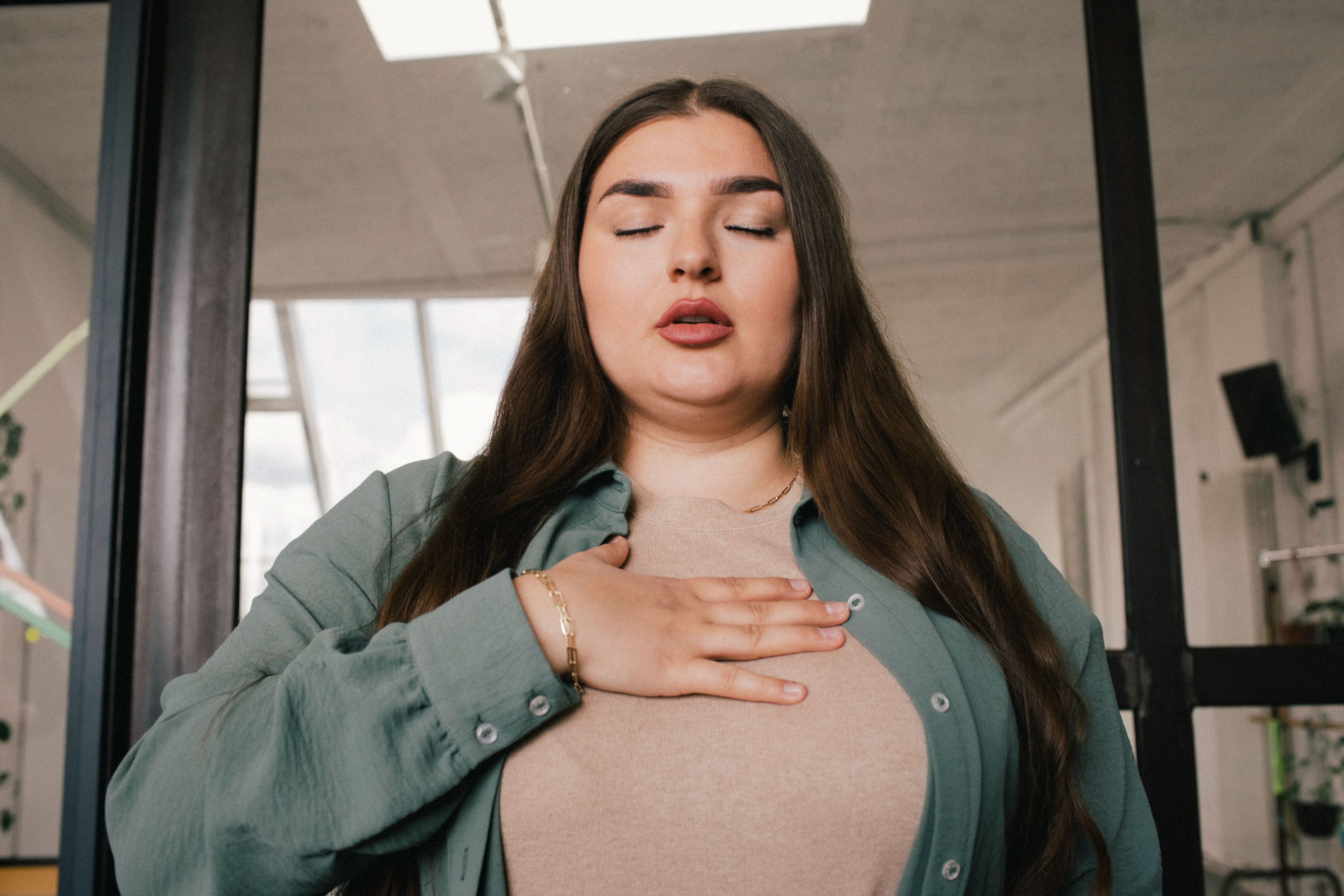 En person står med lukkede øyne, en hånd på brystet, virker rolig og reflekterende, noe som antyder mindfulness eller dyp pust