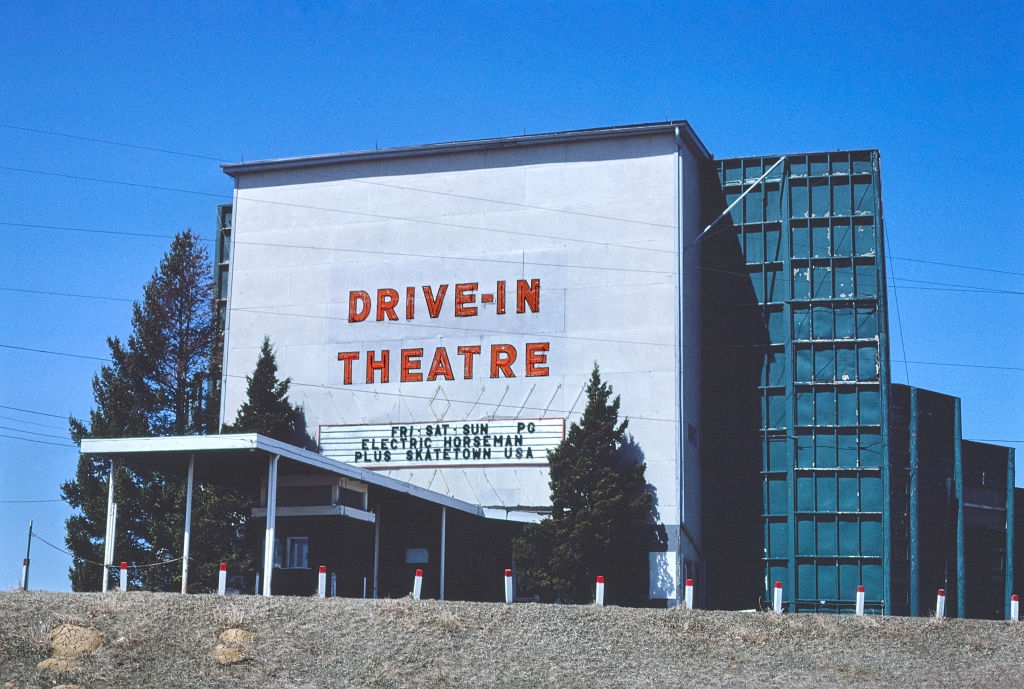 Drive-in theater screen with marquee listing films "Electric Horseman" and "Skatetown, USA," set against a clear sky