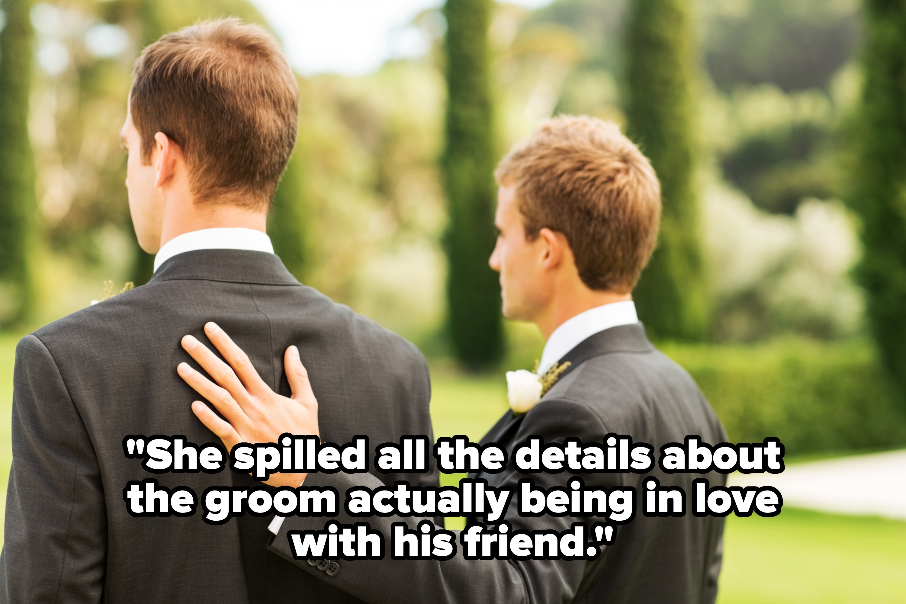 Two men in suits with one resting a hand supportively on the other's shoulder, standing outdoors in a scenic garden setting