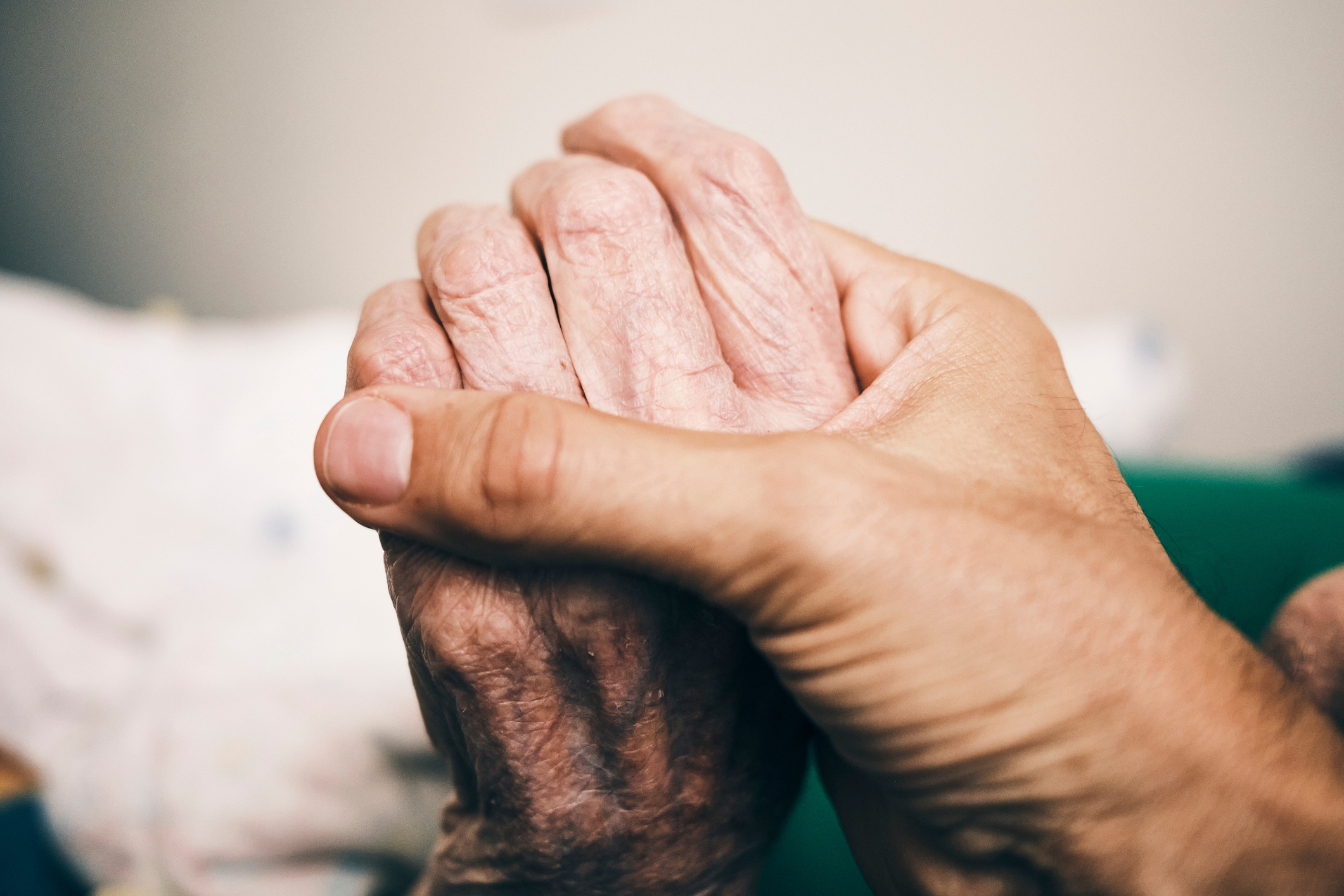 Two hands gently hold an elderly person's hand in a comforting gesture