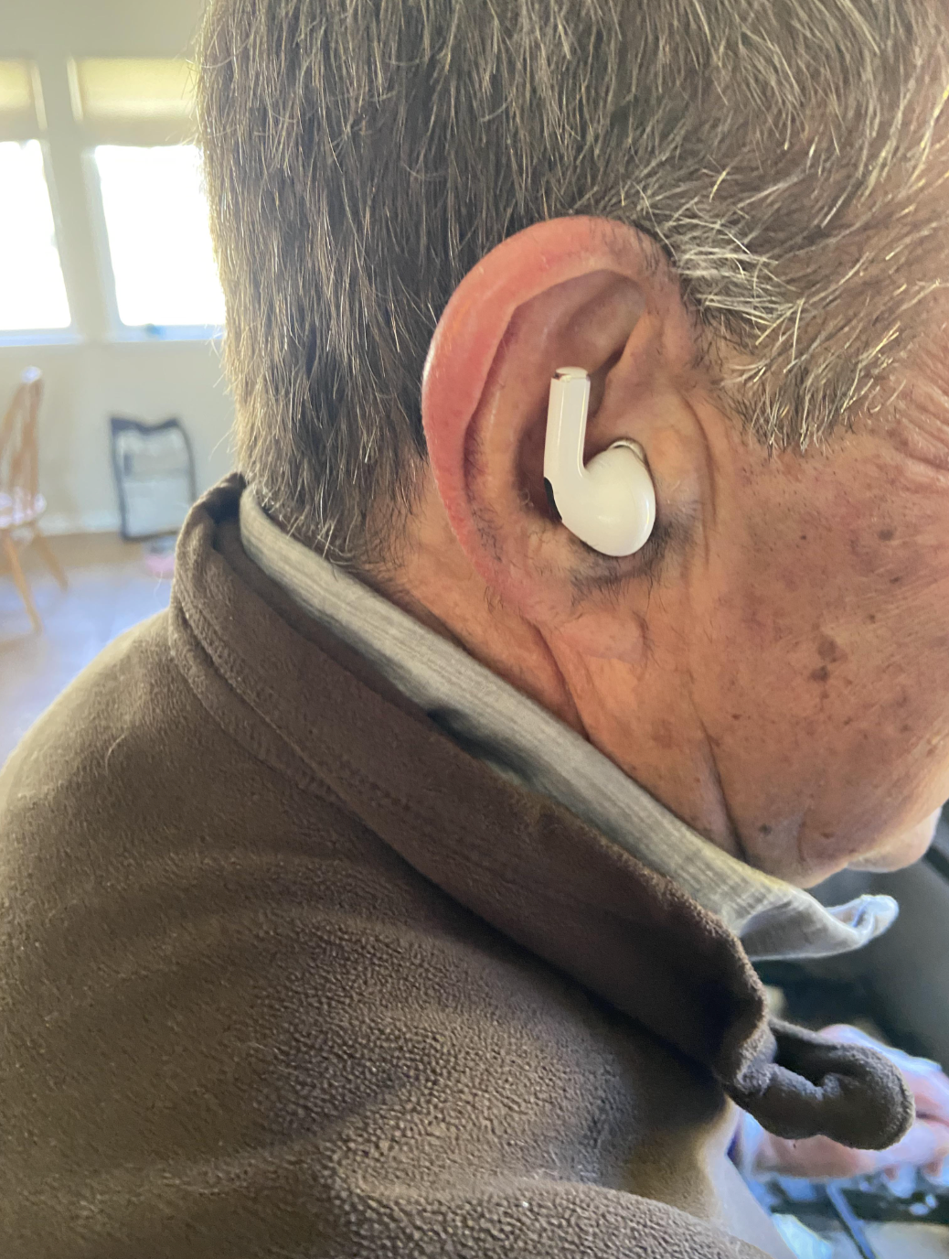 Elderly man humorously wearing an upside-down corded phone handset as an earbud in his ear