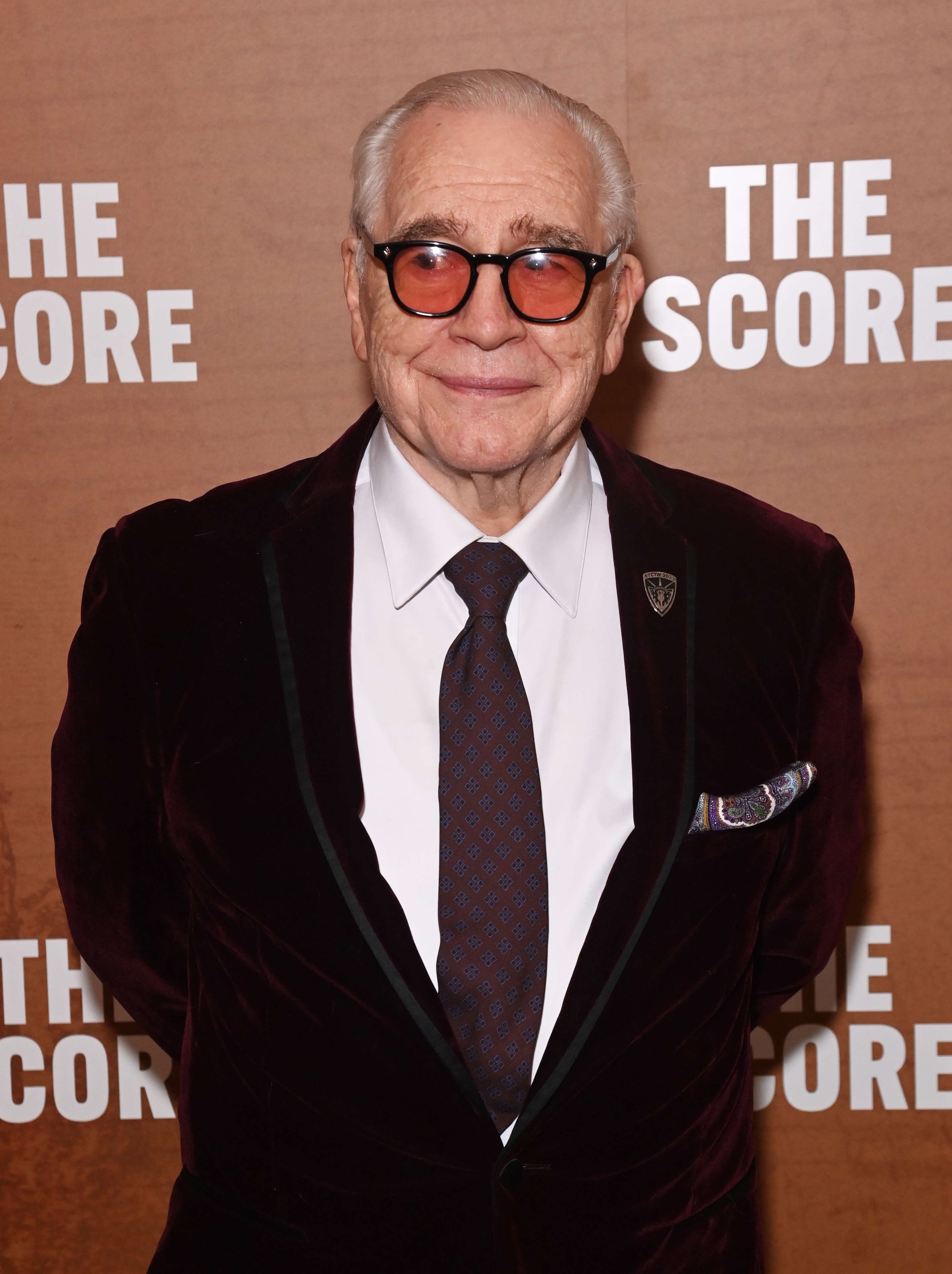 Man in a velvet suit and tie on a red carpet, posing for photos at a media event