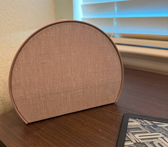 A semi-circular purse with a woven texture sits connected  a array  adjacent  to a tablet, successful  beforehand   of a model   with closed blinds