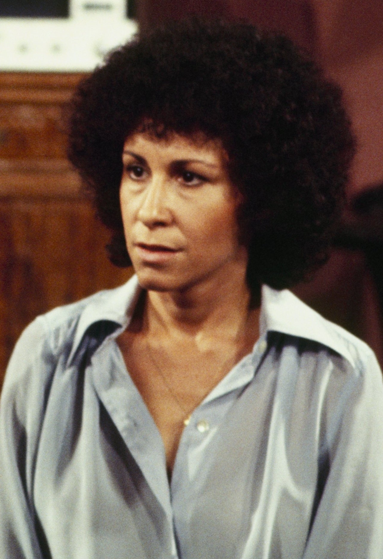 Two people seated, one in a suit and the other in a blouse, engaged in a serious conversation in a domestic setting