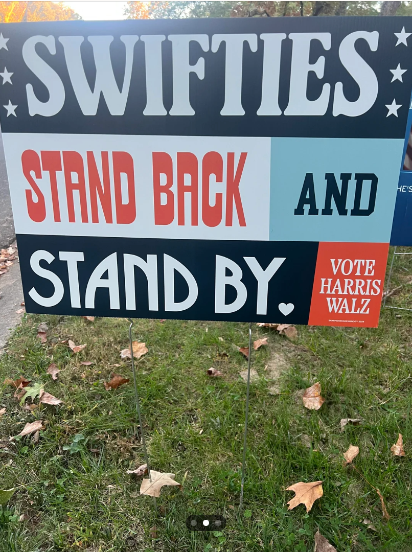 Sign parodying a political slogan reads: "Swifties stand back and stand by. Vote Harris Walz" with star accents