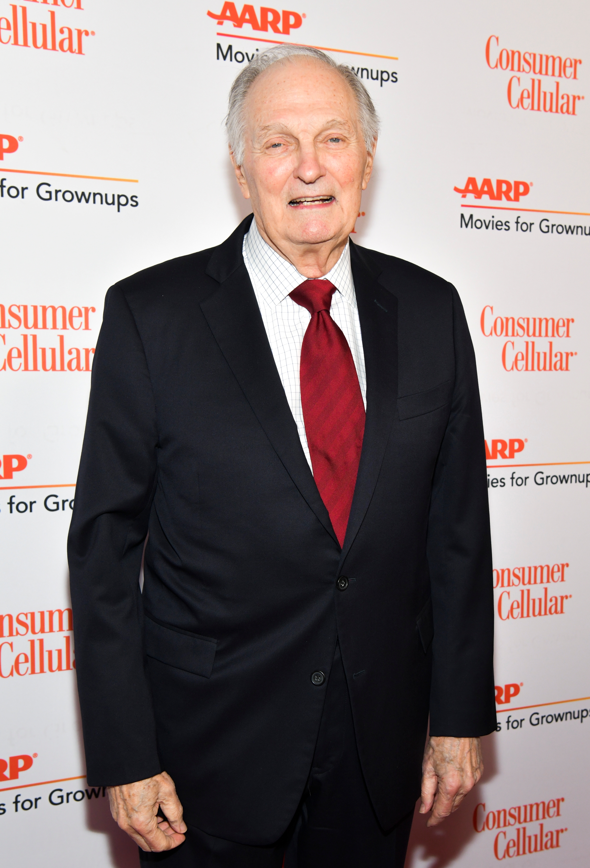 Man in a suit with a red tie on a red carpet at an AARP event