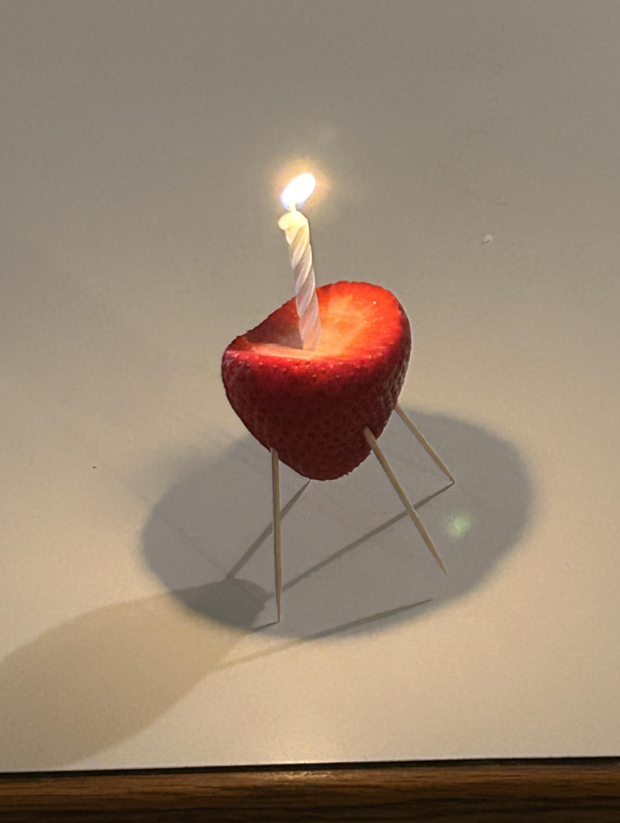 A strawberry half with a lit candle on top, supported by toothpicks, resembling a mini grill
