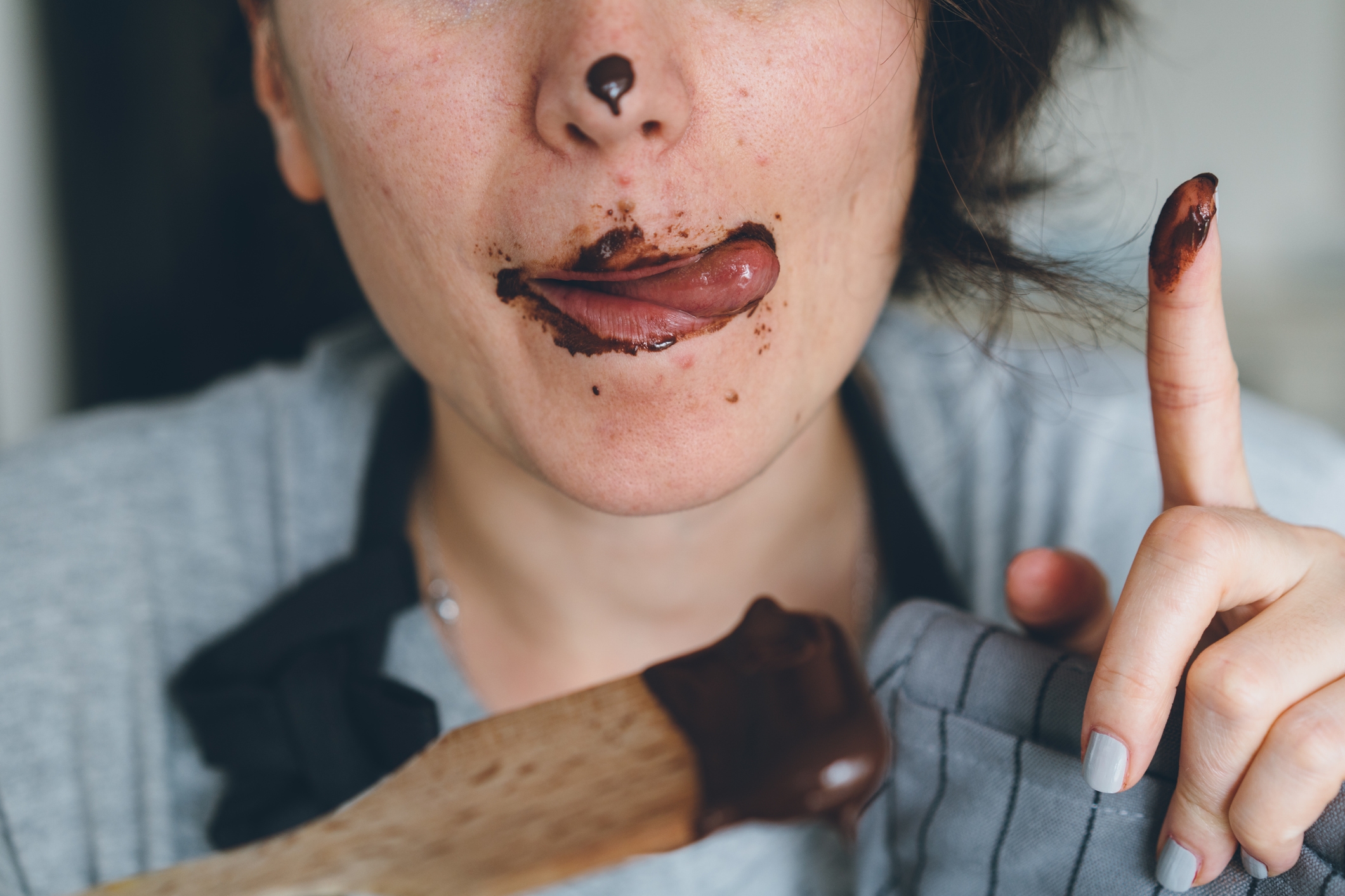 Person som slikker sjokolade av leppene og fingeren, holder et sjokoladebelagt redskap med et lekent uttrykk