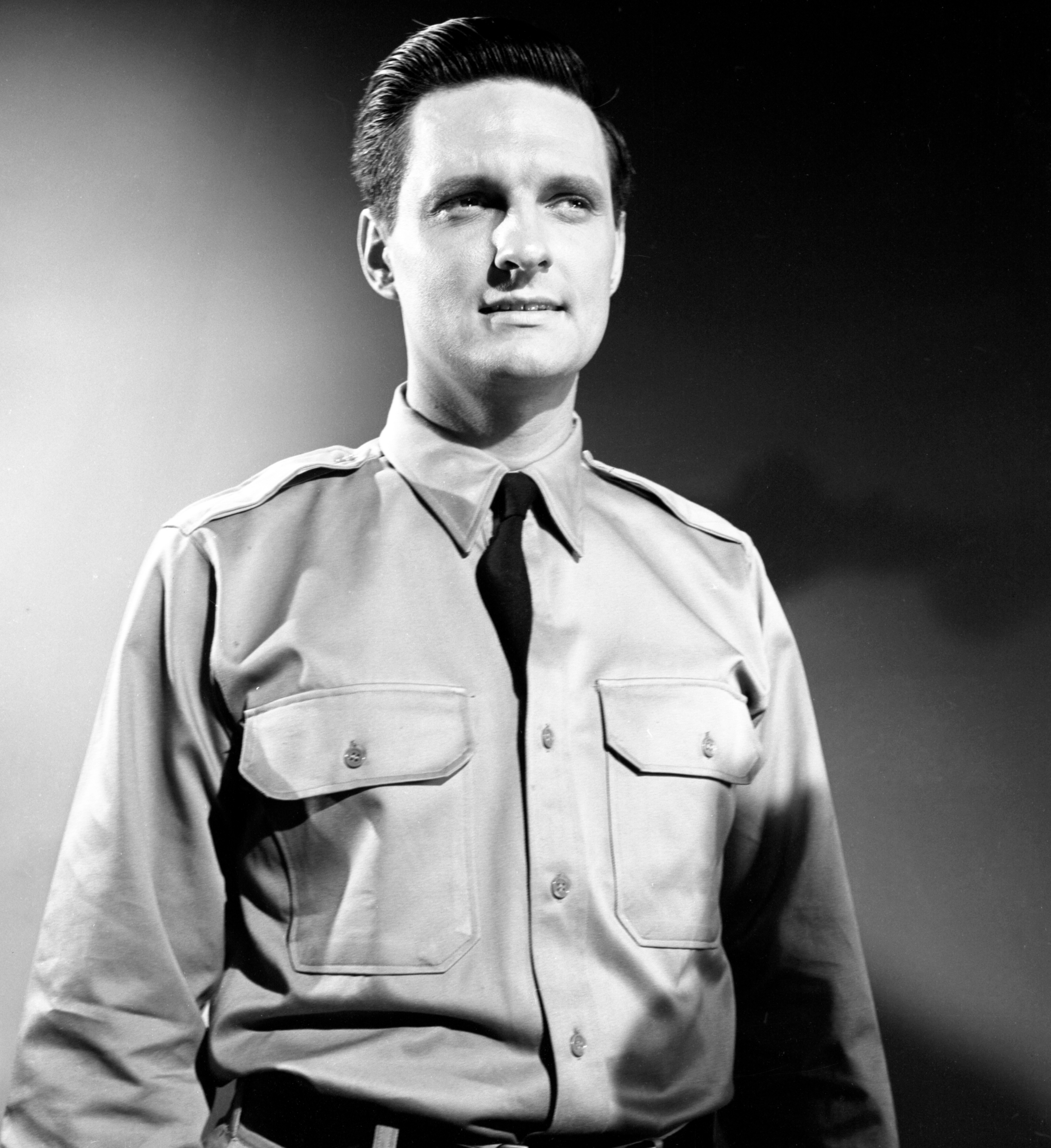 Person in military-style uniform with buttoned shirt and tie, facing forward with a confident expression