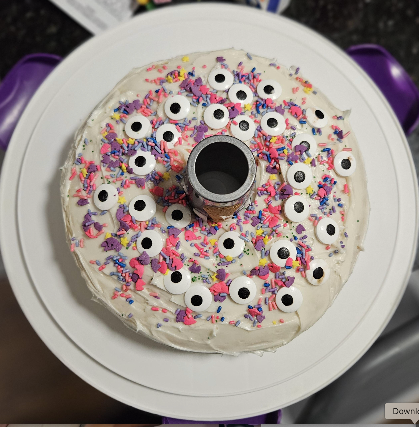 Cake with white frosting, colorful sprinkles, and candy eyes on top, resembling a playful monster theme
