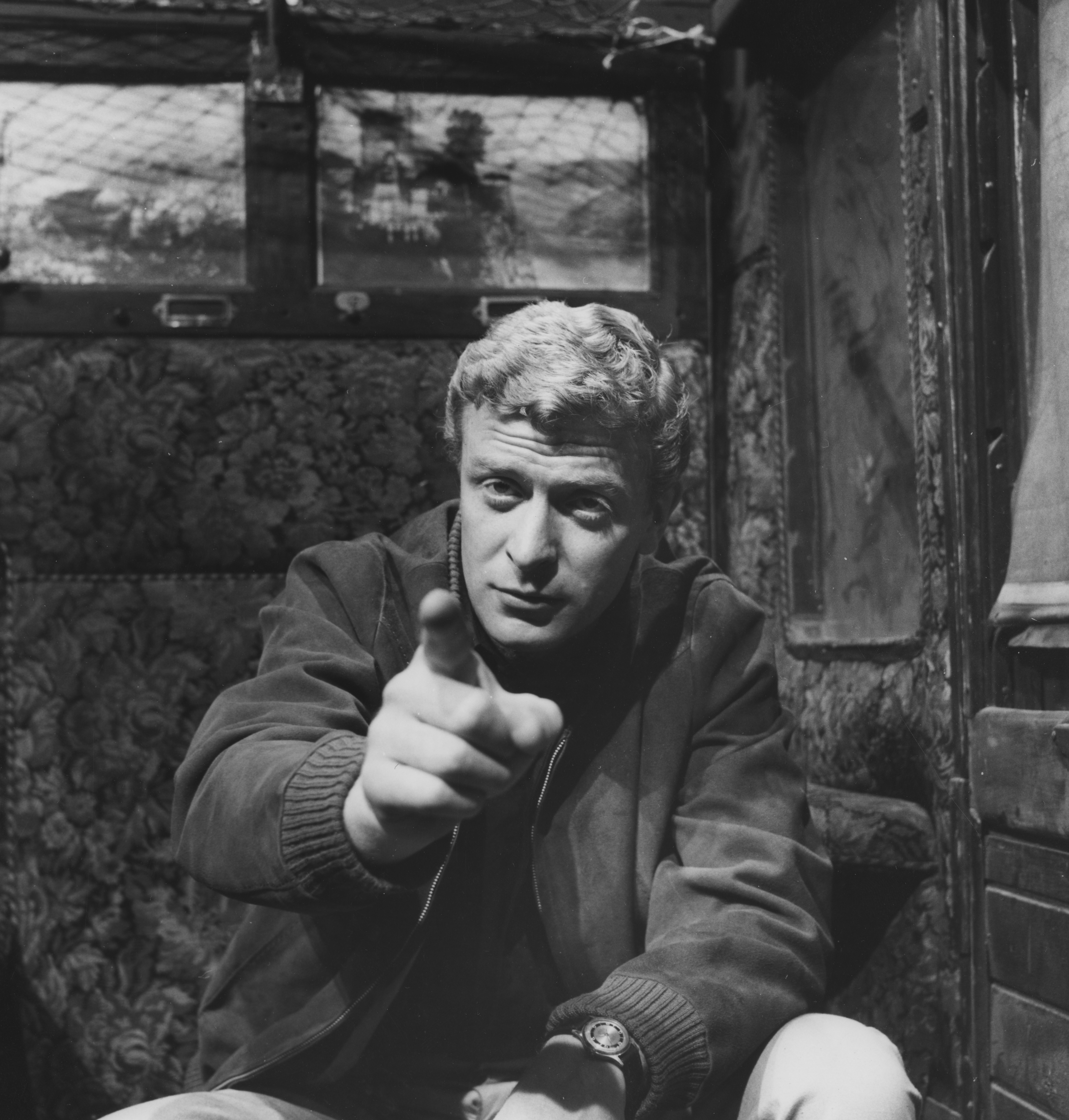 Person in a casual jacket points directly at the camera in a vintage setting