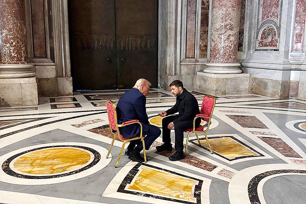 Two men are seated in ornate chairs facing each other in a grand interior with marble floors and columns