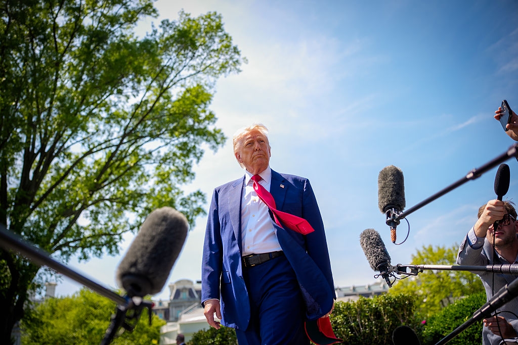 Person in a suit and tie walks outside, surrounded by microphones, likely being interviewed. The scene suggests a media event or press conference