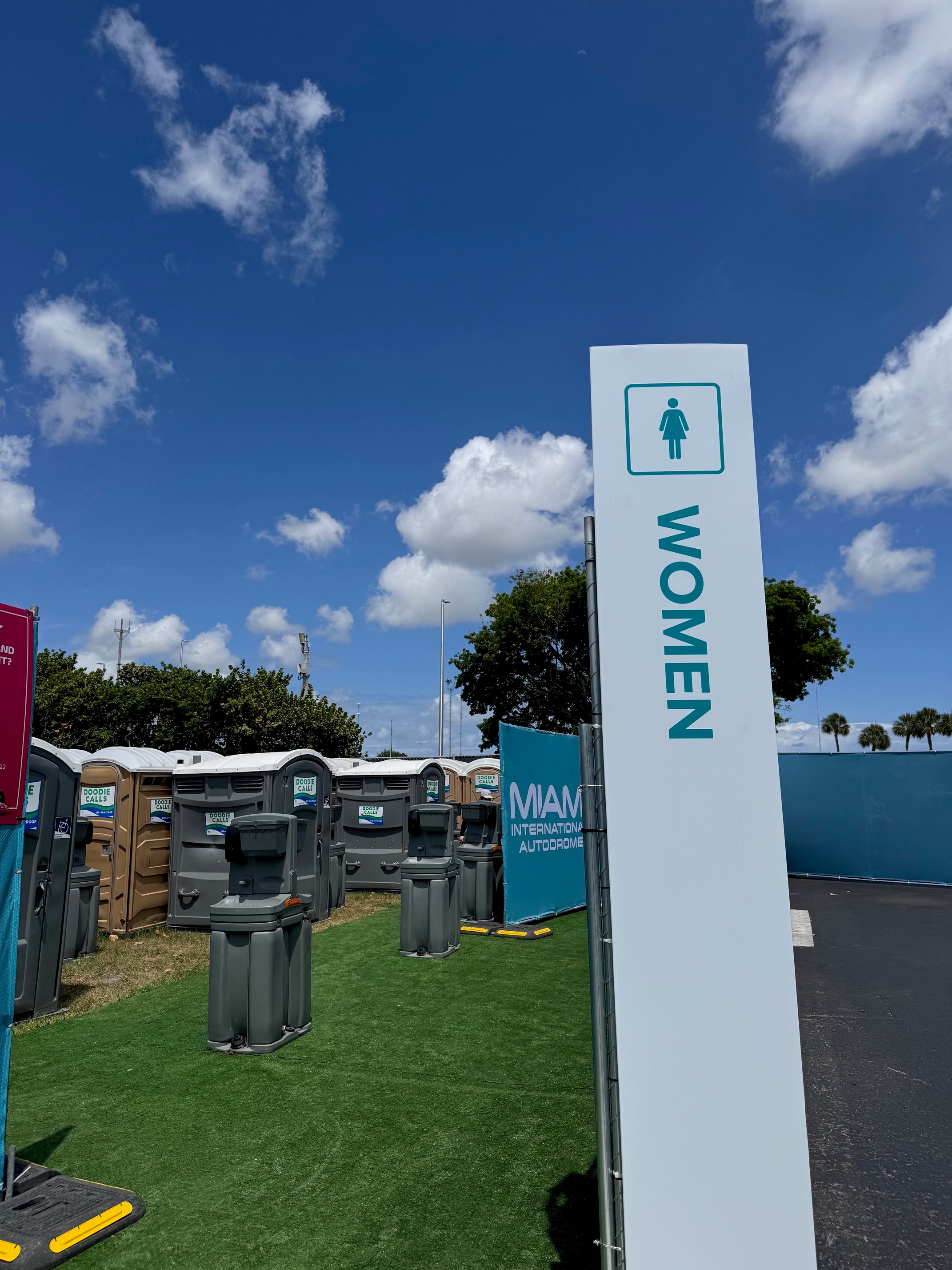 Outdoor portable restrooms at Miami International Autodrome with a "Women" sign and clear sky backdrop