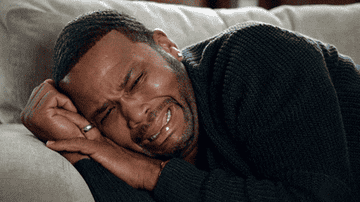 Person lying on a couch, visibly emotional, face scrunched in distress and tears, portraying a moment of intense emotion or reaction